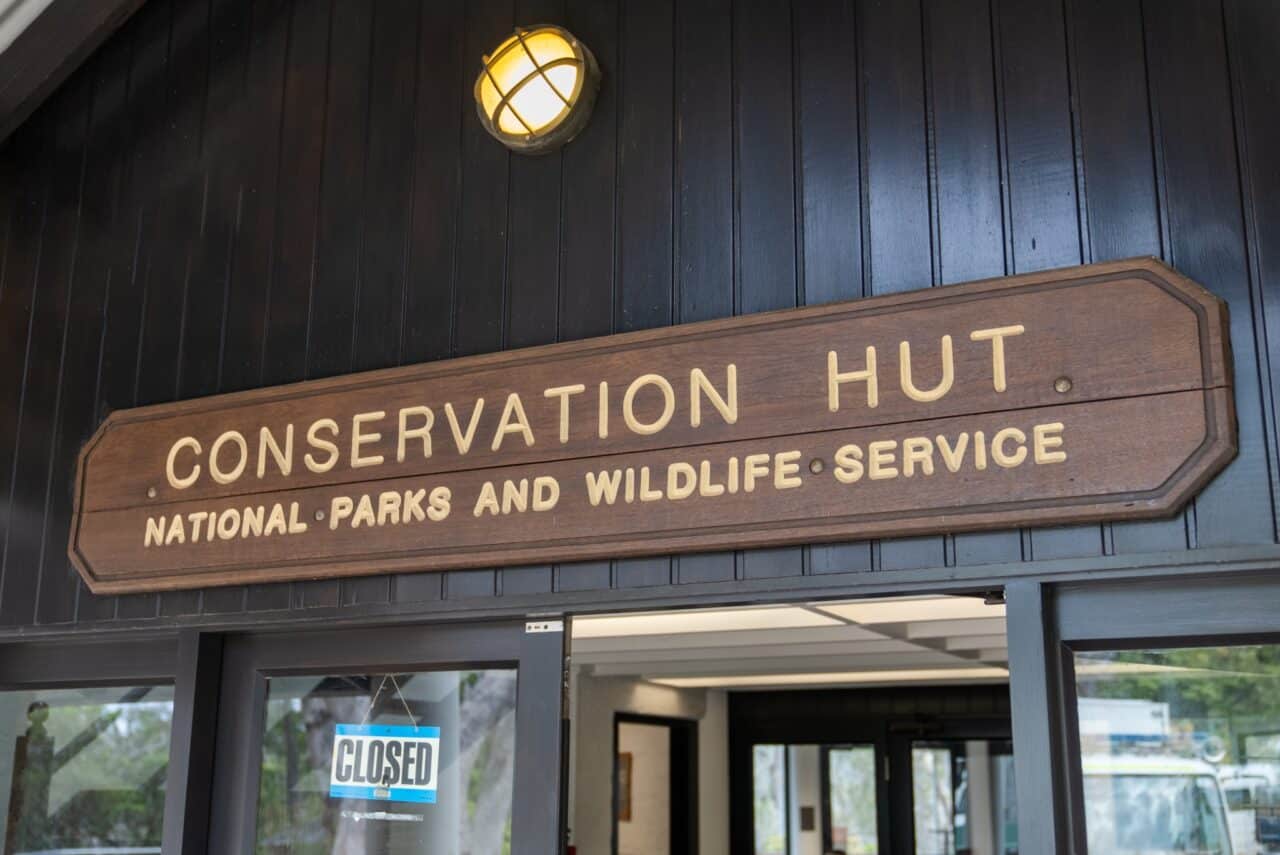 A wooden sign above a door reads "Conservation Hut" with "National Parks and Wildlife Service" below it. A "Closed" sign is visible on the glass door, highlighting the importance of conservation efforts even when access to the hut is restricted.