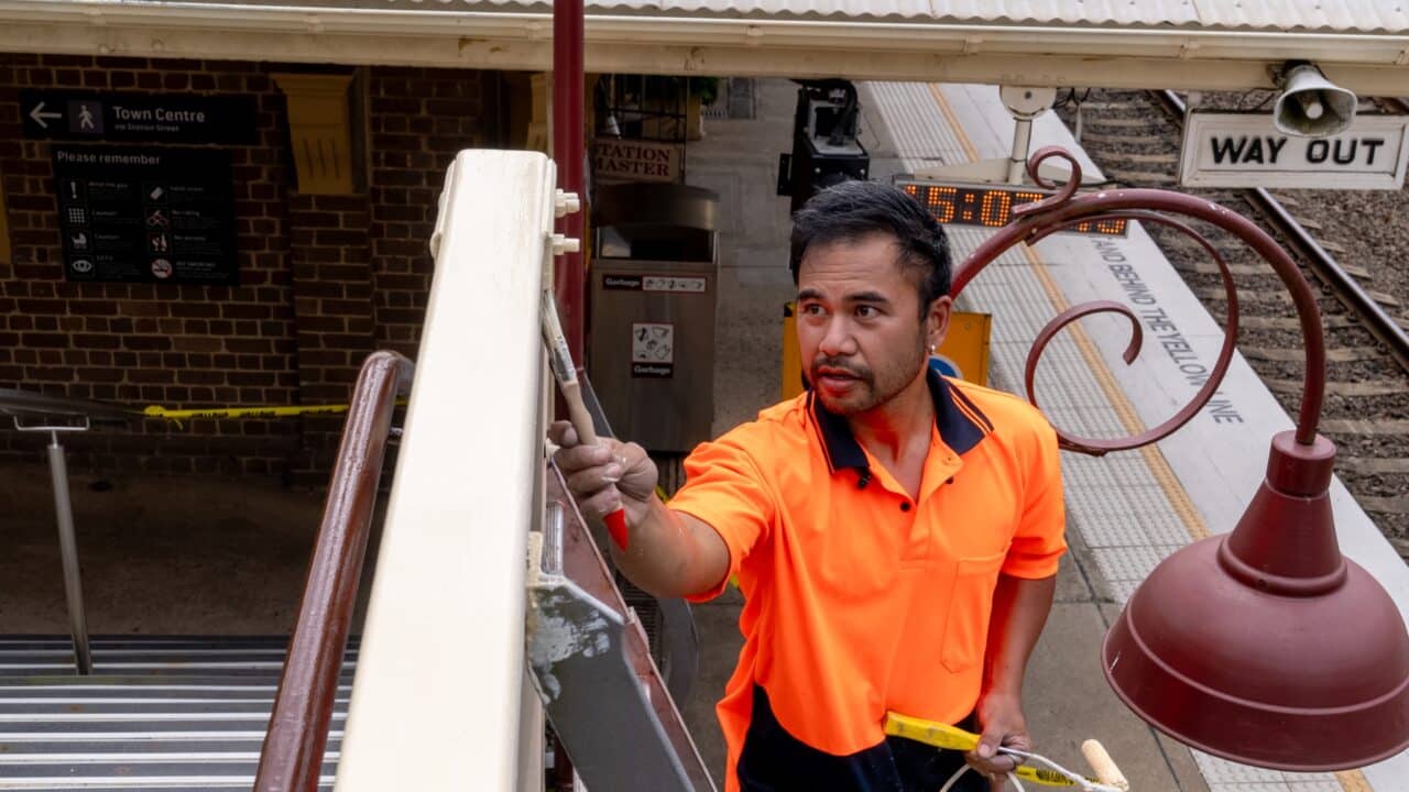 A worker in an orange high-visibility shirt paints a railing as part of the restoration project at Mt Vic Train Station.