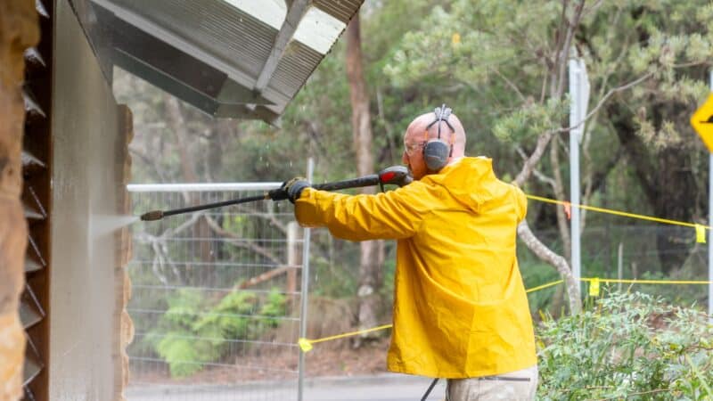 A person in yellow raincoat pressure washing a building's exterior