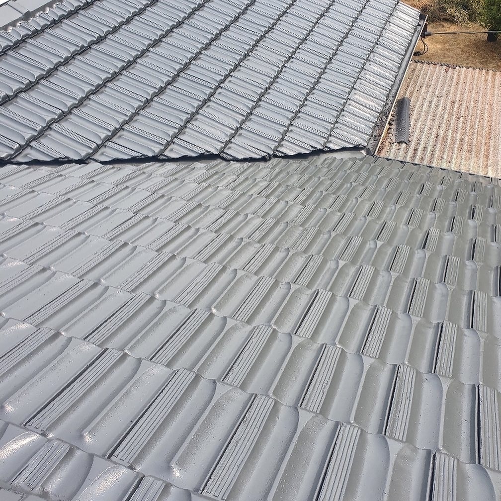 Close-up view of a roof with grey, interlocking ceramic tiles and a section of a different roofing material visible in the background, showcasing the detailed work of expert Roof Repair Services in the Blue Mountains.