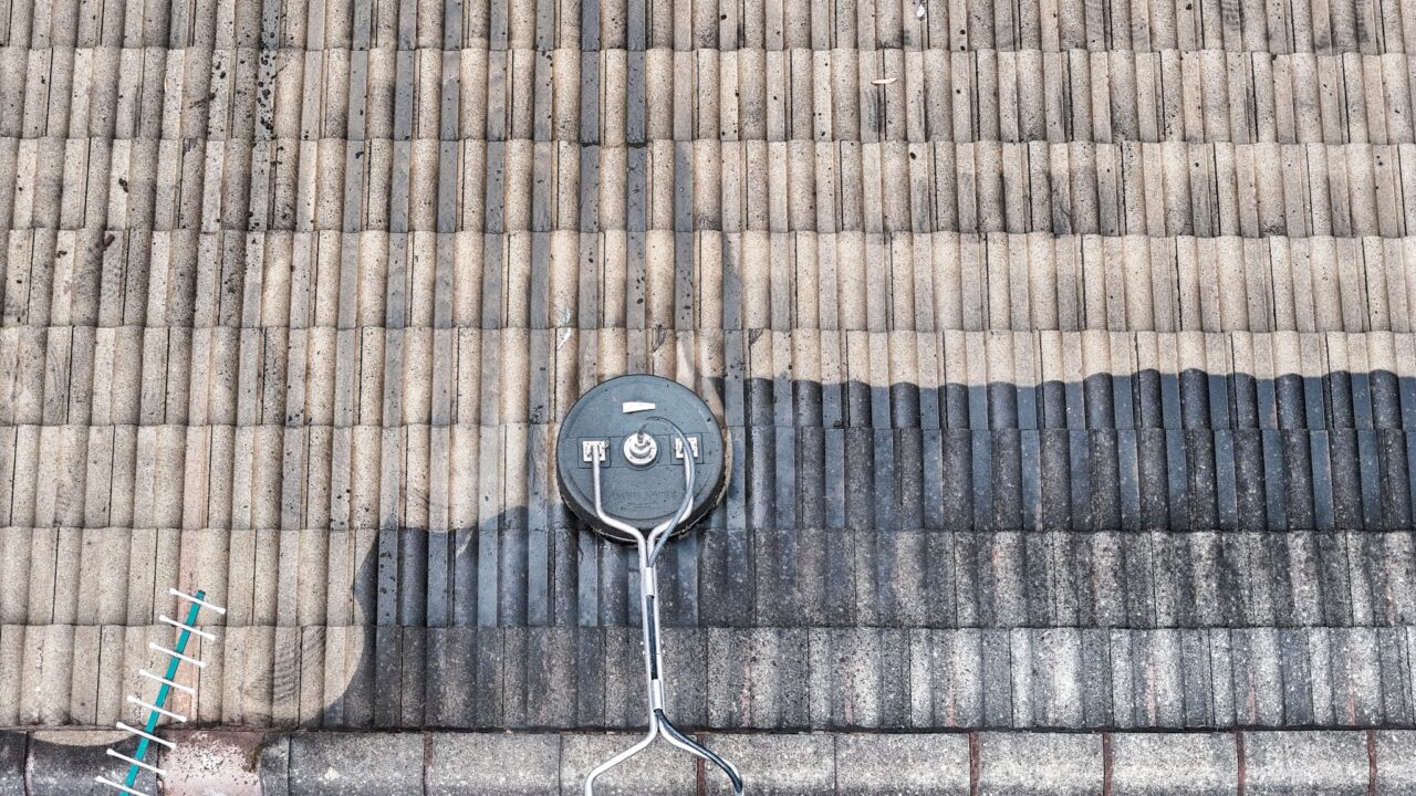 A rooftop in the Blue Mountains shows a clear demarcation of cleaning progress, with one half cleaned and the other dirty. A circular cleaning tool lies on the roof with text and symbols on its surface, highlighting the Roof Cleaning Blue Mountains process.