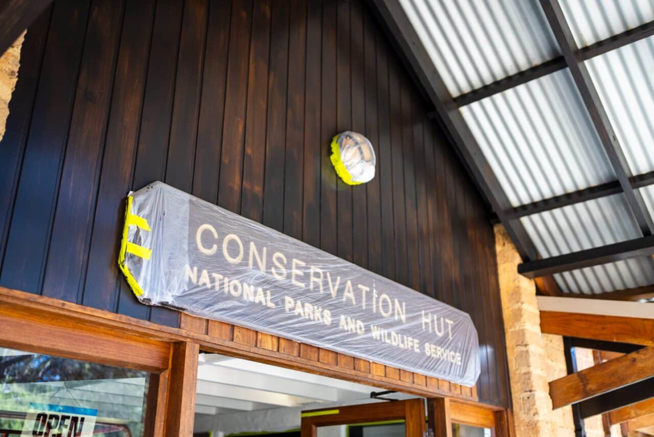 Entrance of a building with a sign reading "Conservation Hut, National Parks and Wildlife Service," partially covered in protective plastic wrap.