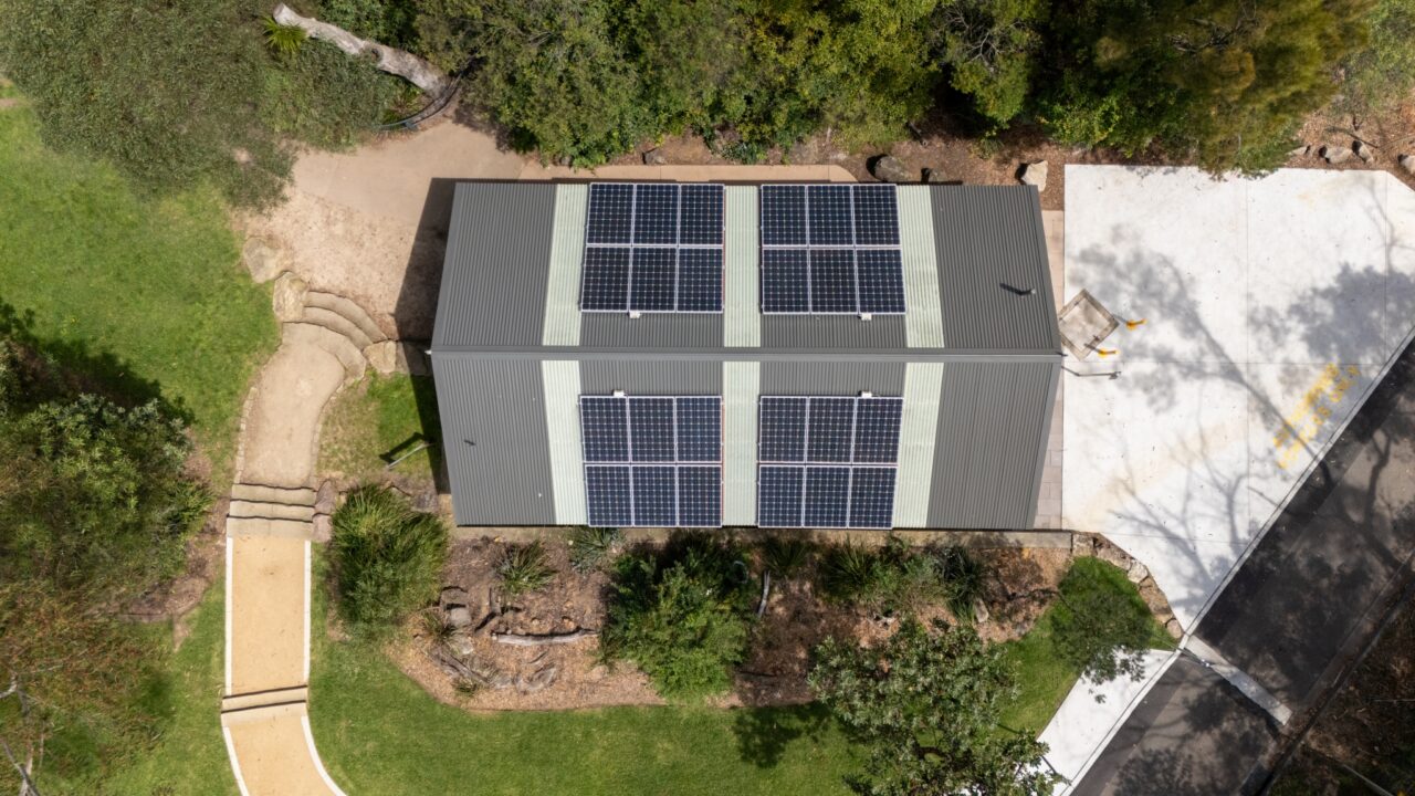 Aerial view of a building with eight solar panels on its roof, nestled amid the greenery and paved area of the Wentworth Falls Lookout, showcasing an impressive Toilet Block Transformation.