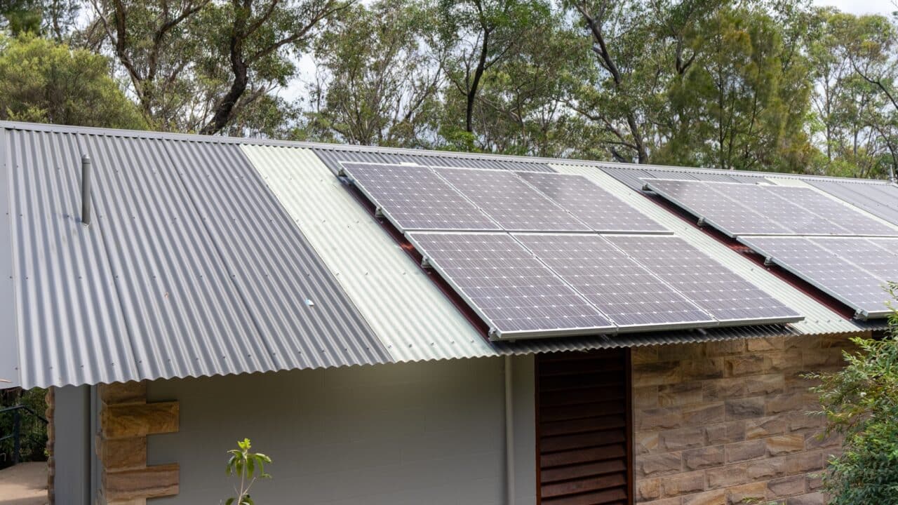 A corrugated metal roof with installed solar panels, part of the Wentworth Falls Lookout project, surrounded by trees and greenery.