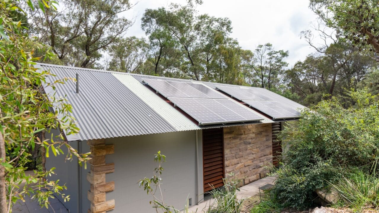 A small house in Wentworth Falls with a corrugated metal roof and solar panels on top, surrounded by trees and greenery.