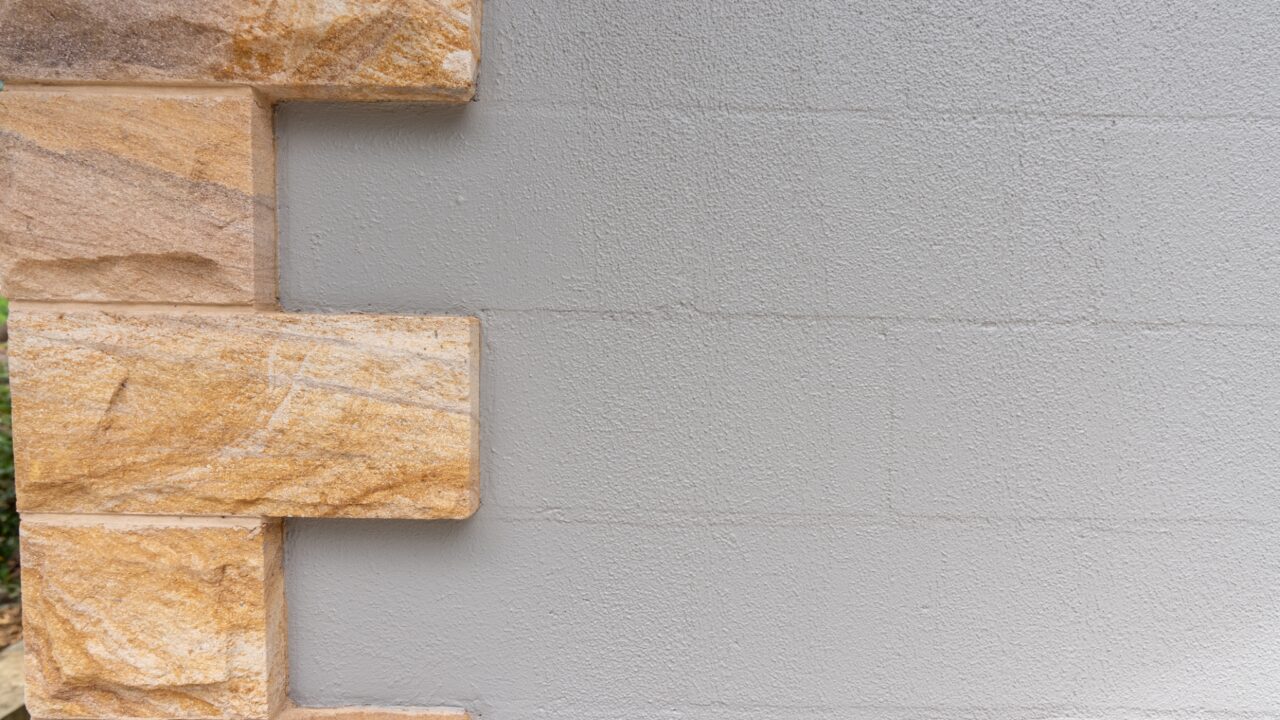 A section of a wall with rectangular light brown stone bricks interlocked on the left and smooth, light gray plaster on the right, reminiscent of the elegant designs found at Wentworth Falls Lookout.