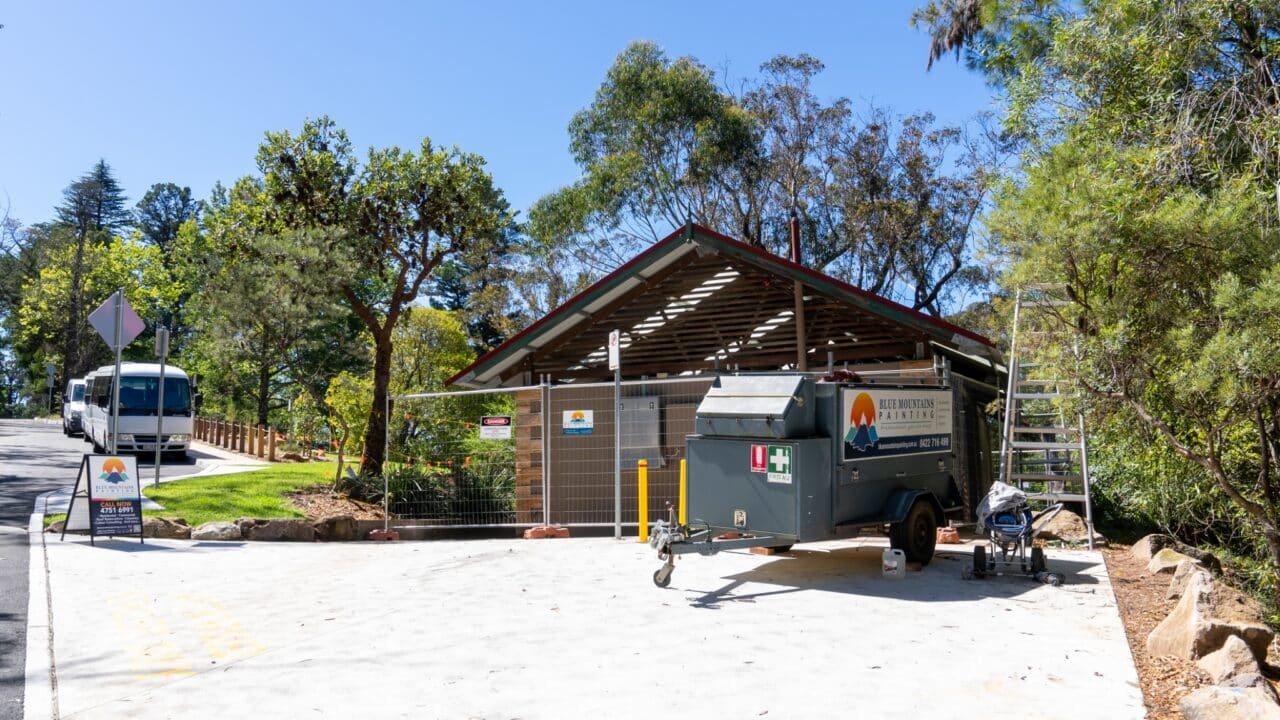 A construction site with a trailer and equipment in front of a building surrounded by trees at Wentworth Falls. A bus is parked on the road nearby, hinting at the Lookout Project in progress.