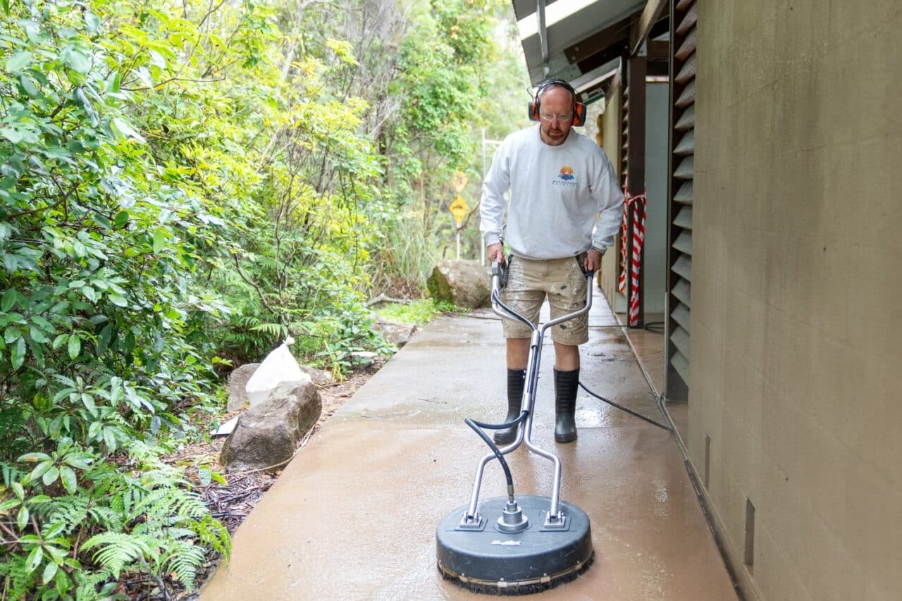 a man with headphones pressure cleaning a patio surrounded by lush greenery